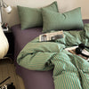 A green and gold striped duvet cover set is displayed on a purple bed, with a lamp visible in the background.