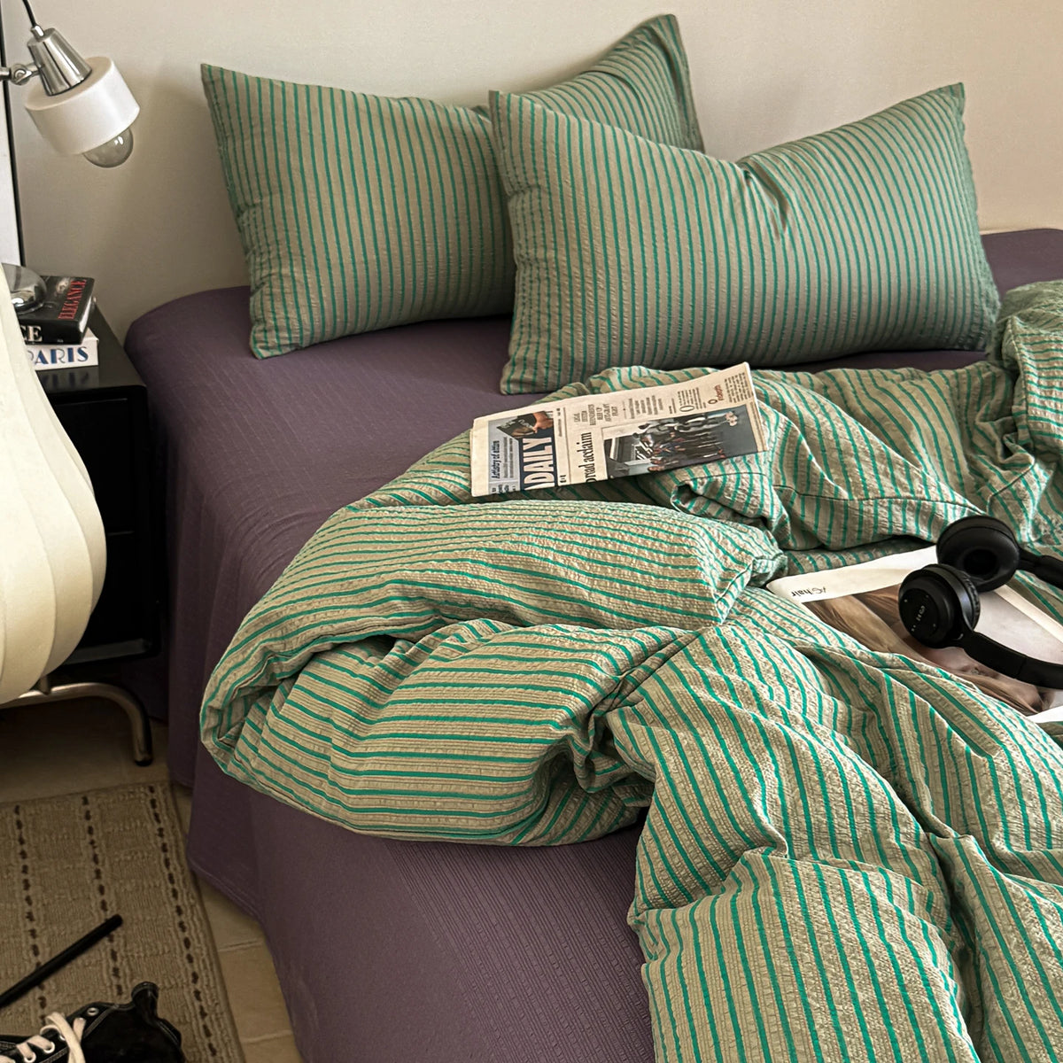 A green and gold striped duvet cover set is displayed on a purple bed, with a lamp visible in the background.