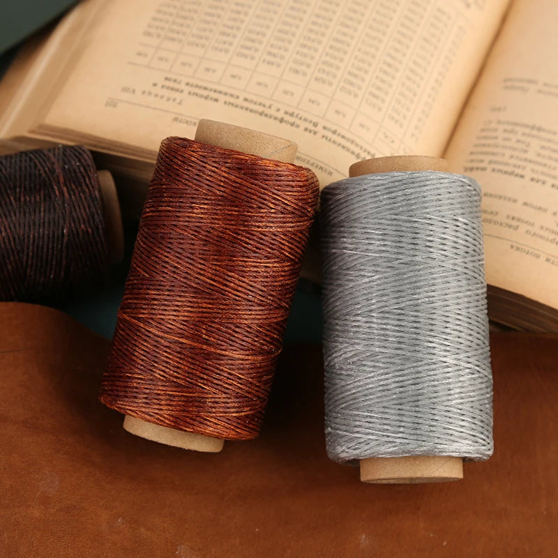 Two spools of waxed thread in copper and gray colors resting on a brown leather surface.