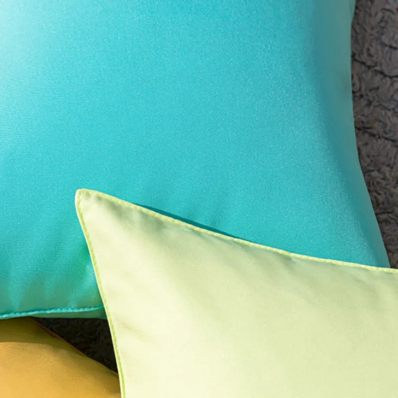 A close-up of three decorative outdoor pillow covers in shades of turquoise, lime green, and yellow.