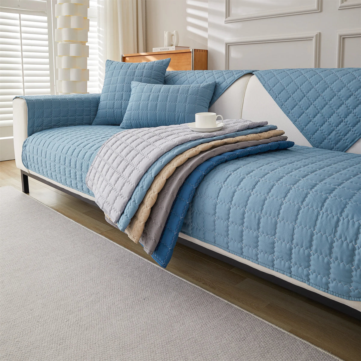 A light blue quilted sofa cover with various textured gray and blue throw blankets on a white sofa.