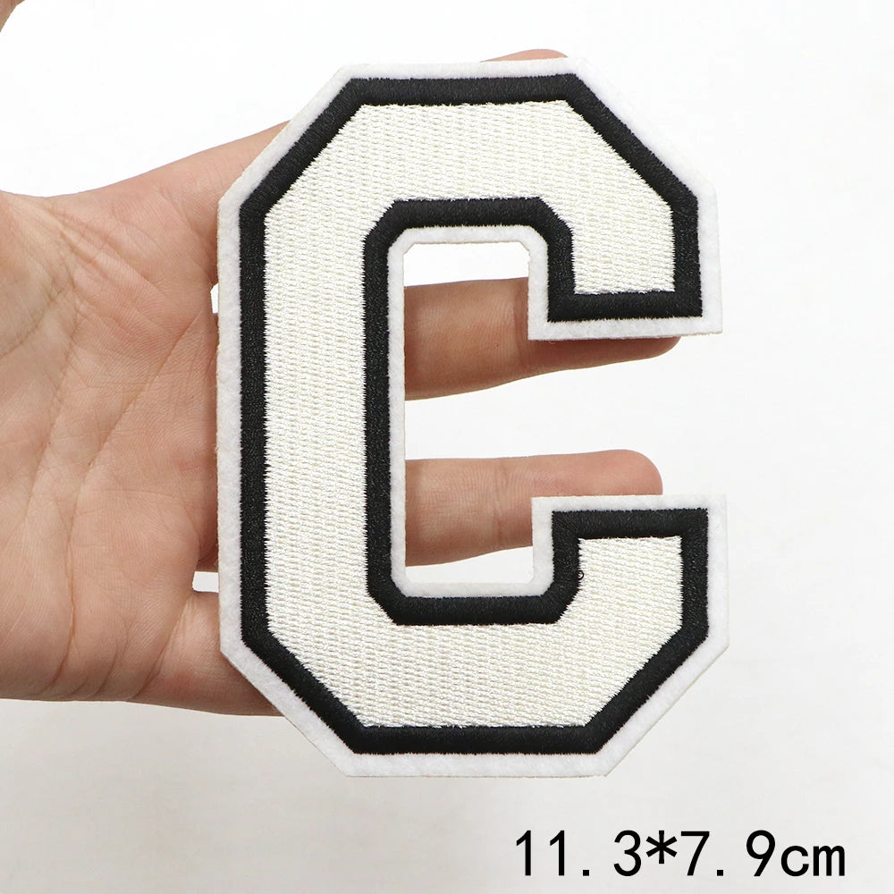 A hand holds a white and black letter C patch for clothing decoration.