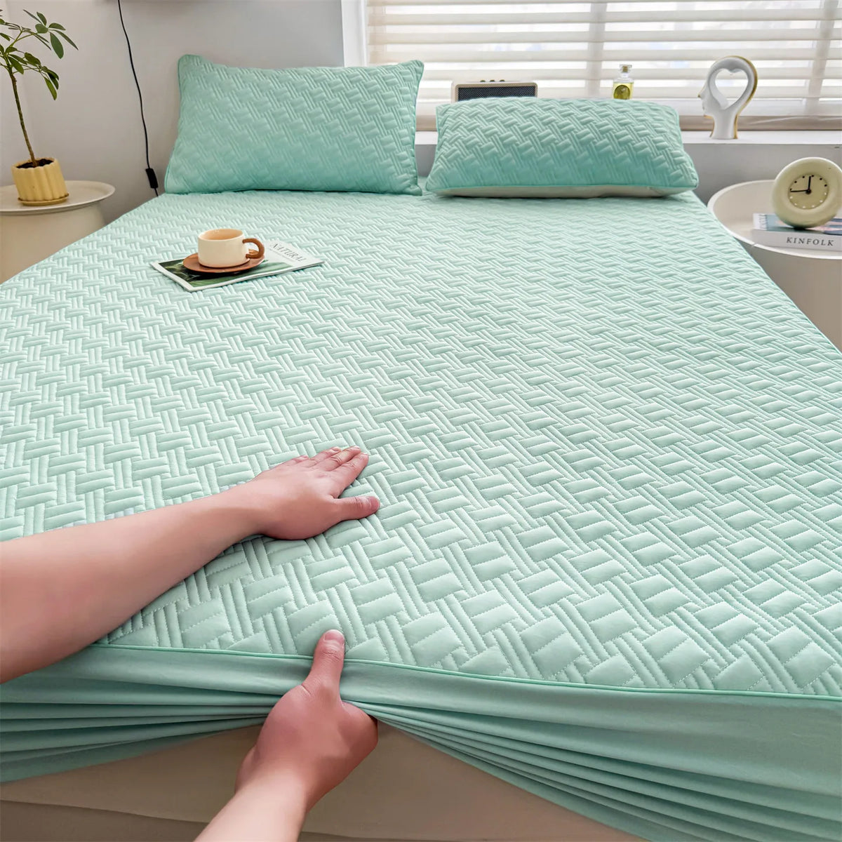 A teal cooling spandex fitted sheet mattress protector is shown on a bed, with a hand touching the fabric.