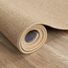 A rolled natural sisal jute rug in a light tan color resting on a wooden surface.