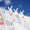 Close-up of white heavy-duty plastic clothespins attached to a piece of colorful, patched fabric against a blue sky.