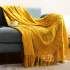 A bright yellow knitted tassel throw blanket draped over a gray sofa.