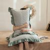 A person is holding a plaid washed cotton pillowcase with ruffled edges against a light background.