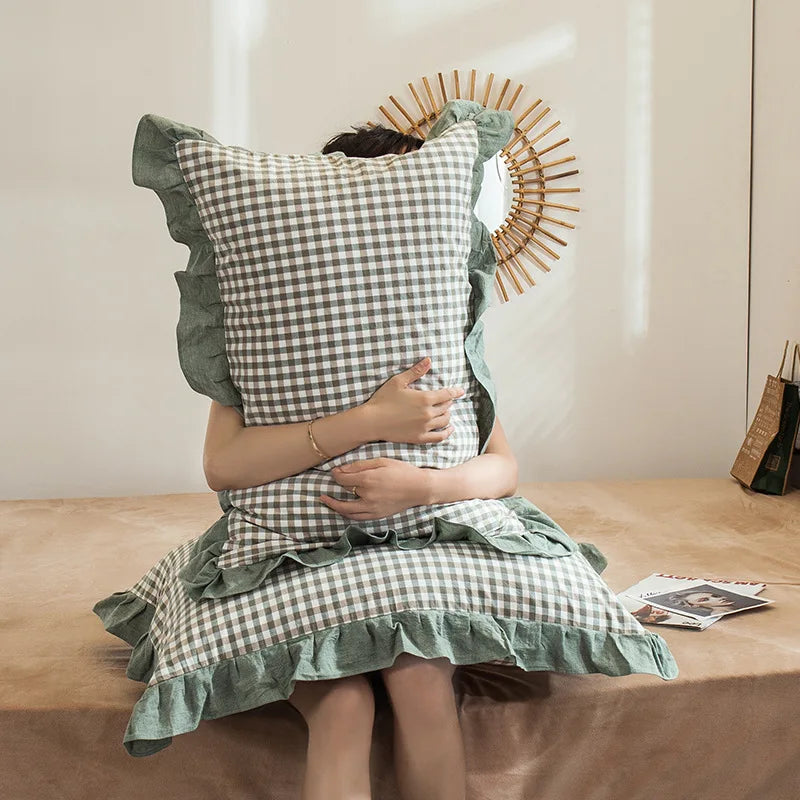 A person is holding a plaid washed cotton pillowcase with ruffled edges against a light background.