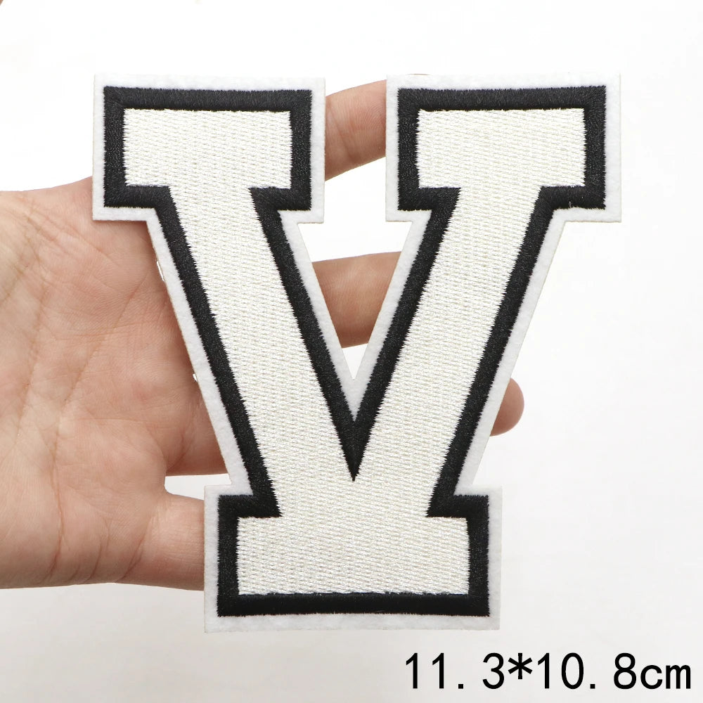 A hand holds a white letter V patch with black outline and stitching.