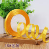 Roll of gold satin ribbon with a central white core and loose ribbons on a wooden surface