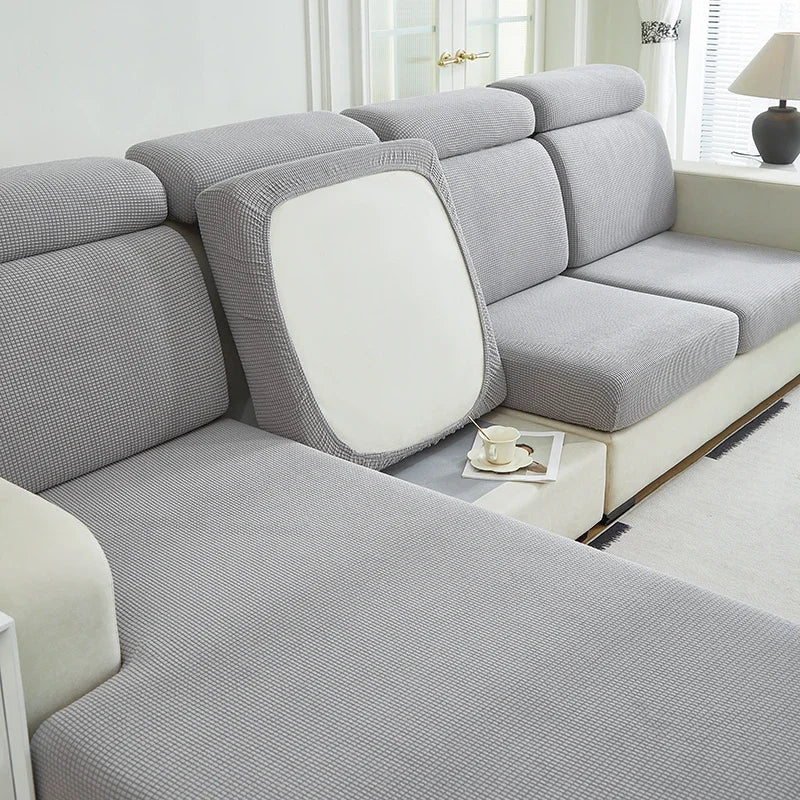 A light gray Jacquard elastic sofa cushion slipcover with a white accent cushion shown in a bright room.
