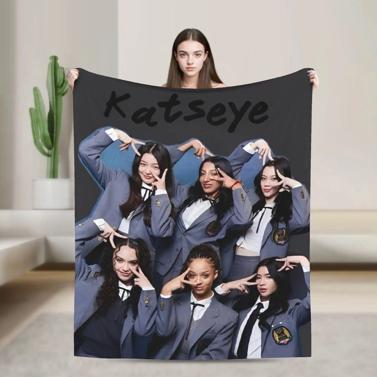 A black blanket featuring a collage of nine young women in matching gray jackets and ties, with the name Katseye written acro