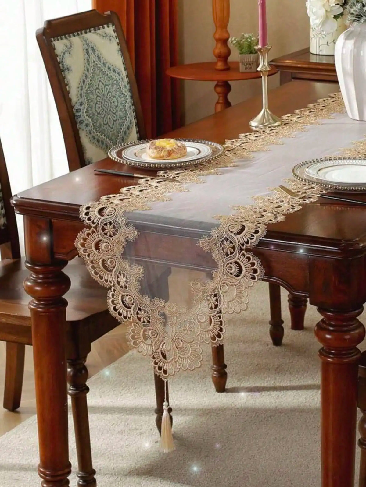 A brown wooden table is set with an embroidered mesh lace table runner and a plate.