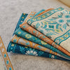 Stack of patterned textile sofa covers featuring blue, teal, and orange embroidery on a gray fabric.