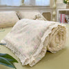 A rolled light pink quilt blanket with a floral print is displayed on a green surface.