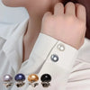 A close-up of pearl button pins in various colors and finishes being held by a hand against a white shirt.