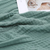 A soft sage green pure cotton gauze throw blanket draped over a surface next to a white card.