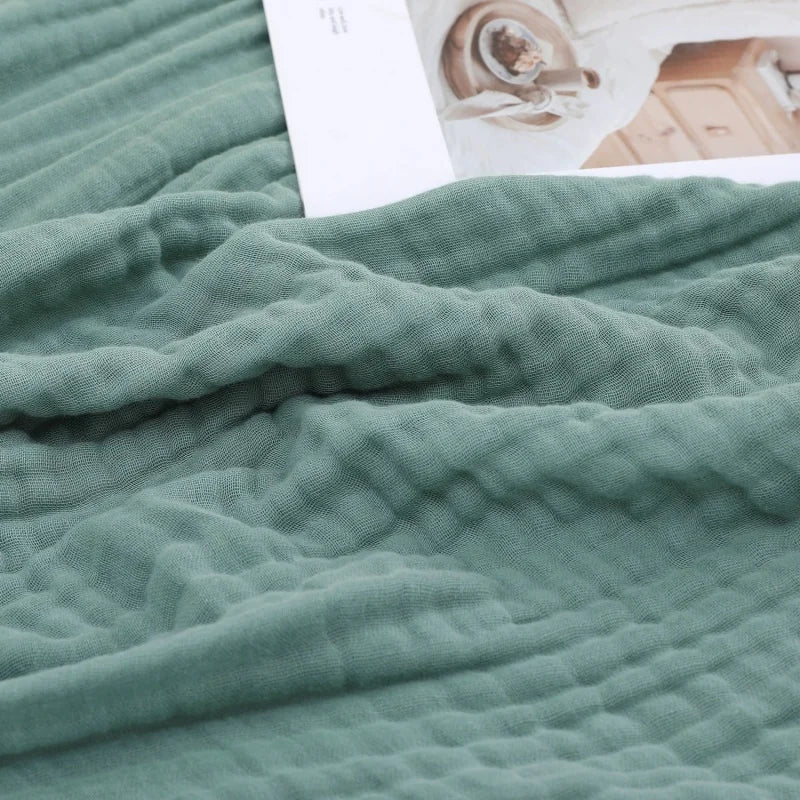 A soft sage green pure cotton gauze throw blanket draped over a surface next to a white card.