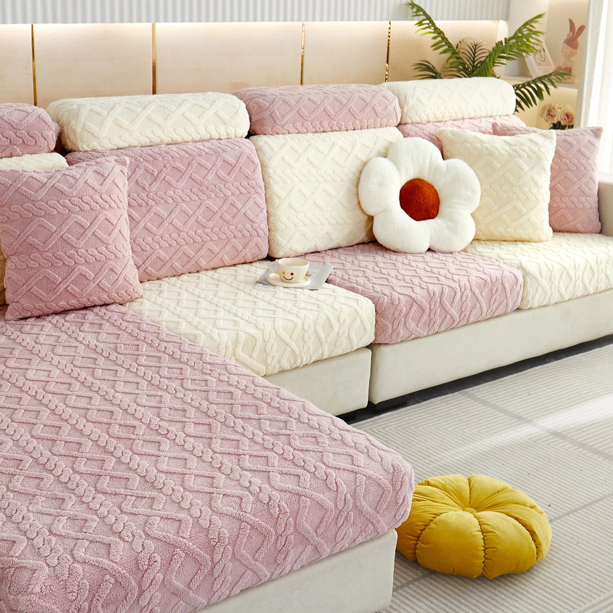 A plush velvet sofa cover in pink and cream tones with quilted cushions and a yellow decorative ball.