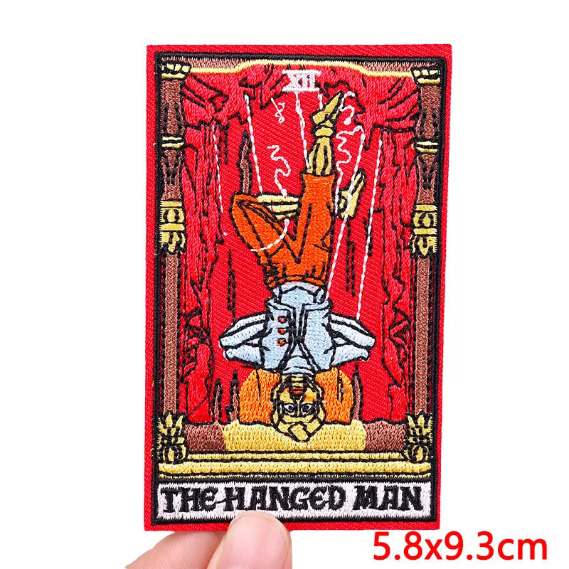 An embroidery patch depicting The Hanged Man with a rose skull motif in red and gold thread.