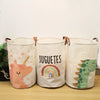Three white canvas storage baskets with cartoon prints of a unicorn, rainbow, and dinosaur.