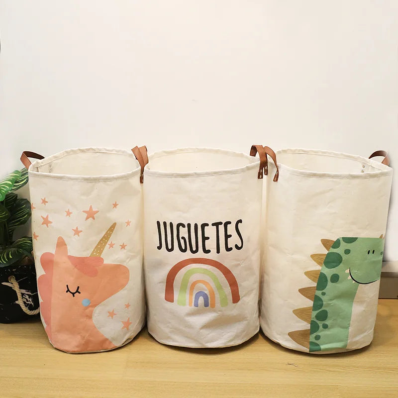Three white canvas storage baskets with cartoon prints of a unicorn, rainbow, and dinosaur.