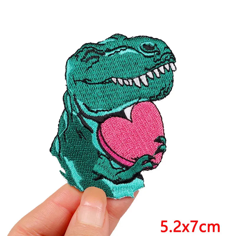 A teal cartoon dinosaur embroidered patch with a pink heart on it.