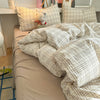 A beige plaid duvet cover set with matching pillowcases and a small white stuffed animal on a bed.