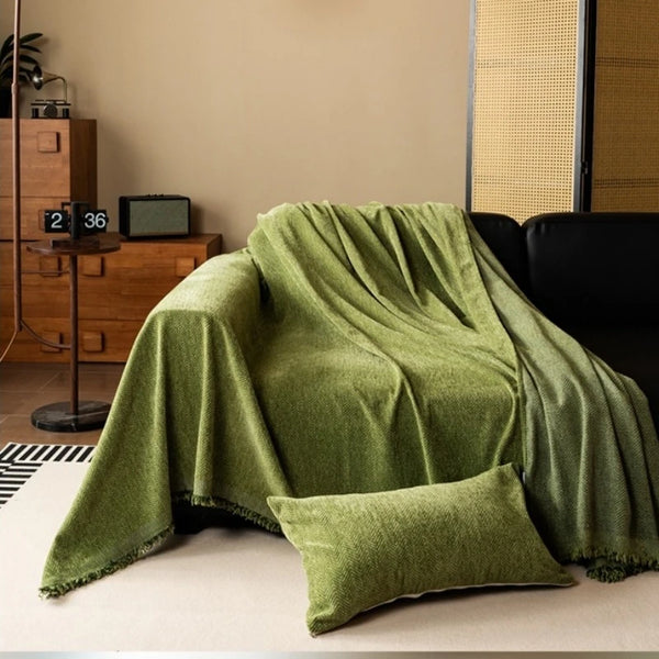A draped olive green chenille sofa cover with fringed edges resting on a light-colored surface.