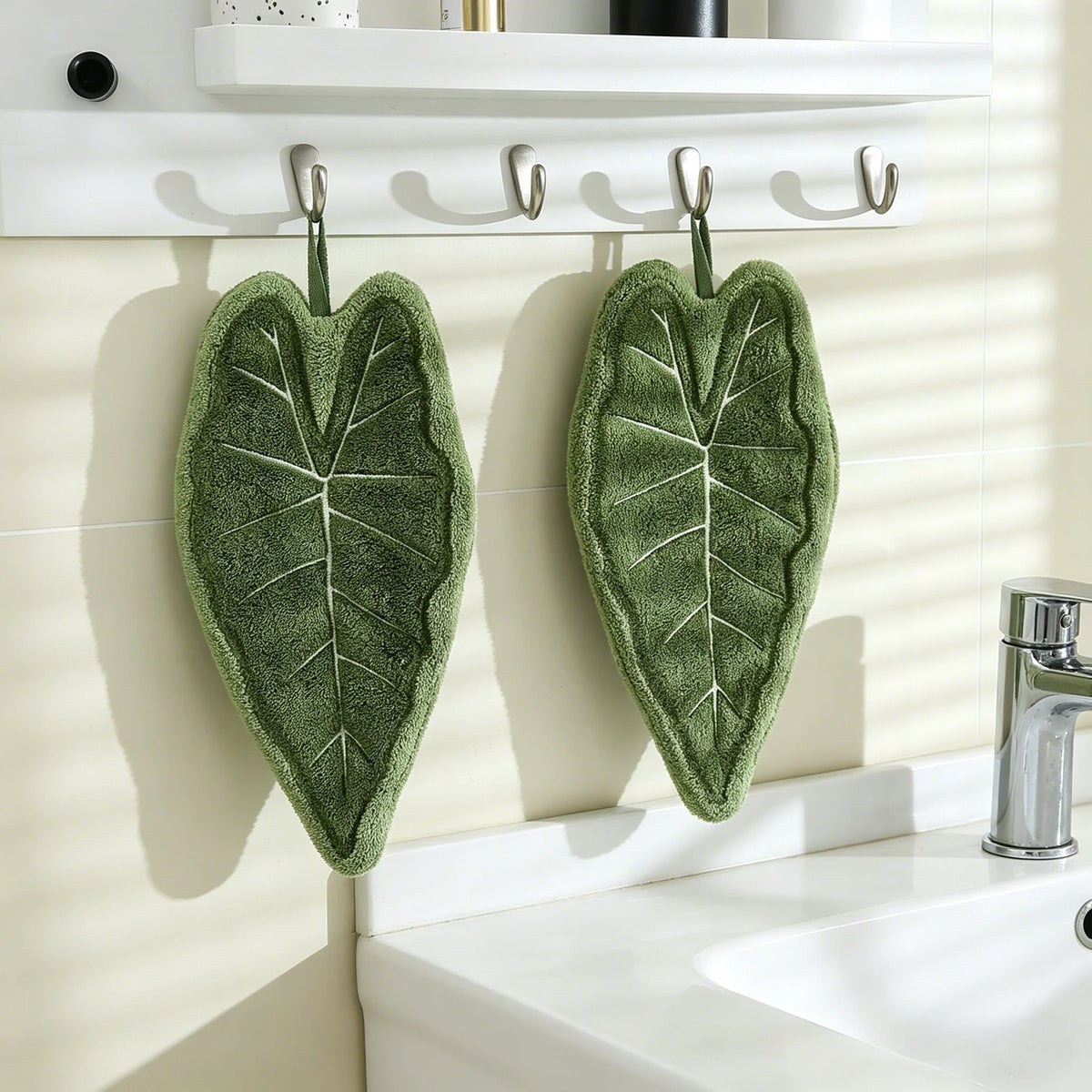 A green decorative banana leaf hanging hand towel displayed on a white shelf above a sink.