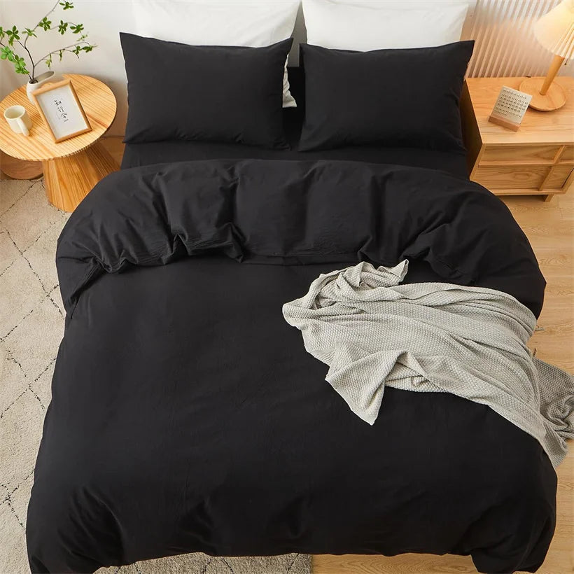A black minimalist duvet cover with matching pillows and a gray throw blanket on a bed.