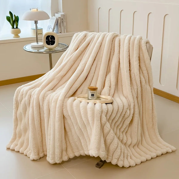 A thick, cream-colored fluffy blanket draped over a surface in a bright room.
