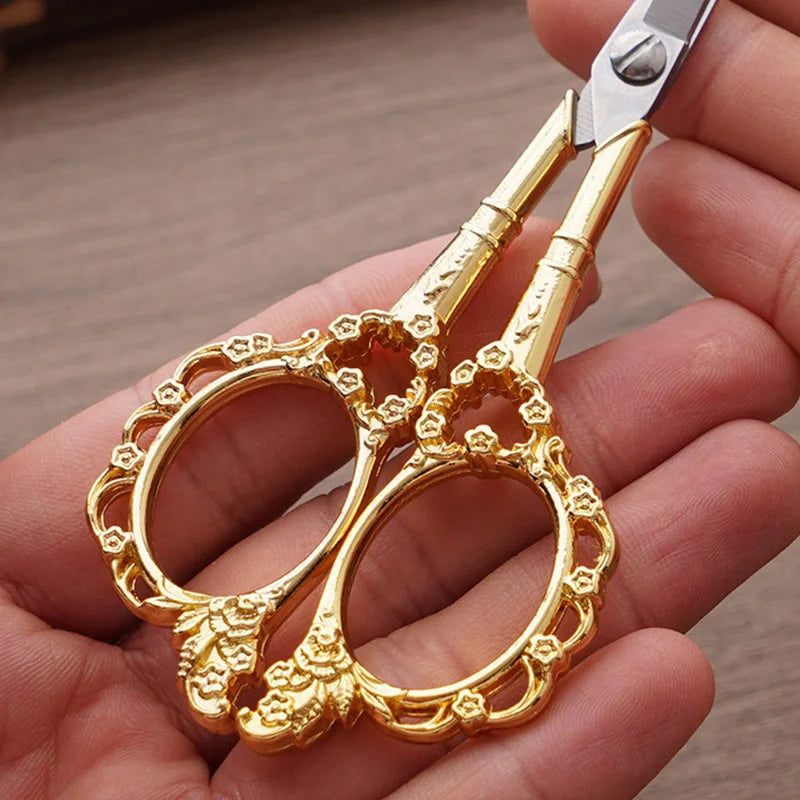 A pair of ornate gold-colored crafting scissors held in a person's hand.