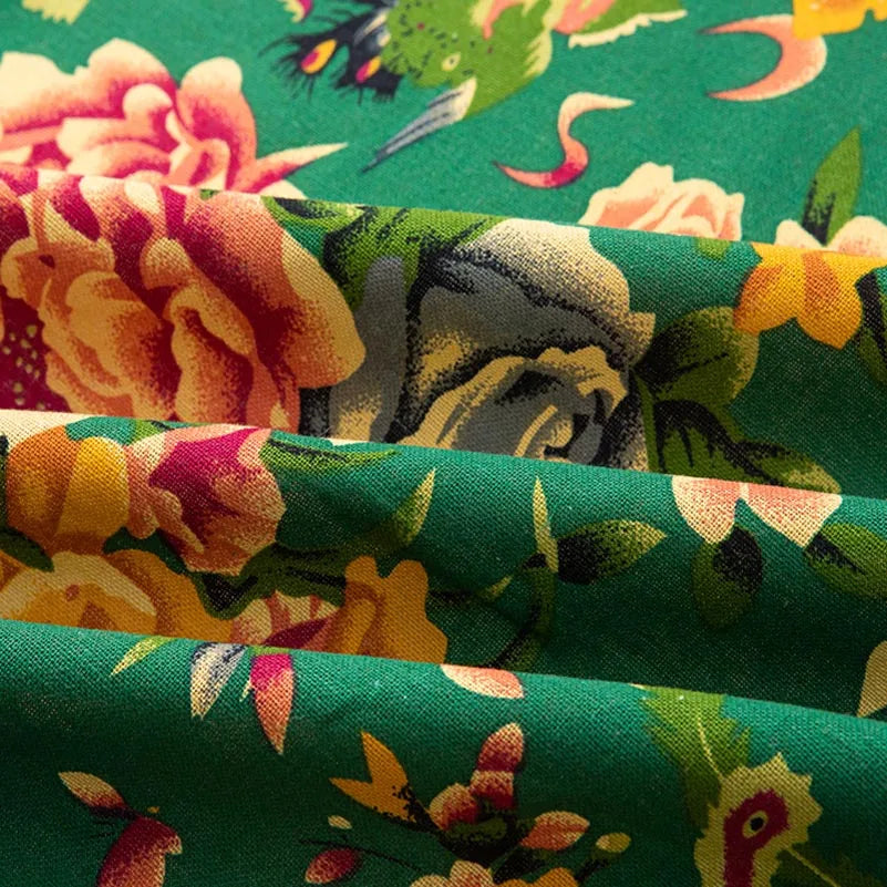 Close-up of green linen fabric with a floral print featuring roses and leaves in shades of yellow, pink, and cream.