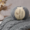 A ball of grey wool thread labeled Wool Thread Delicate and Soft Intimate Warmth resting on a knitted item.
