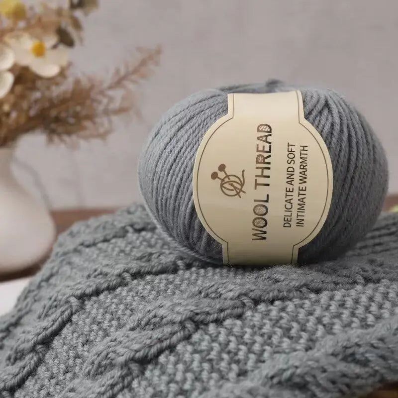 A ball of grey wool thread labeled Wool Thread Delicate and Soft Intimate Warmth resting on a knitted item.