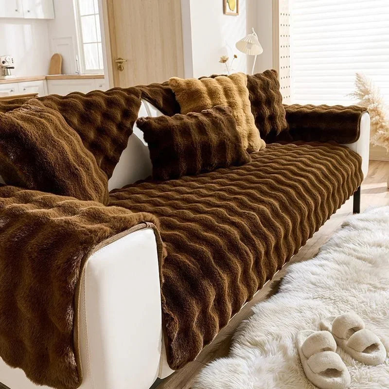 A plush brown rabbit sofa cushion draped with a textured throw on a white sofa.
