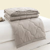 A stack of light gray quilted duvet covers and a folded duvet on a white bed.