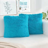 A set of two vibrant turquoise faux fur throw pillows resting on a white sofa.