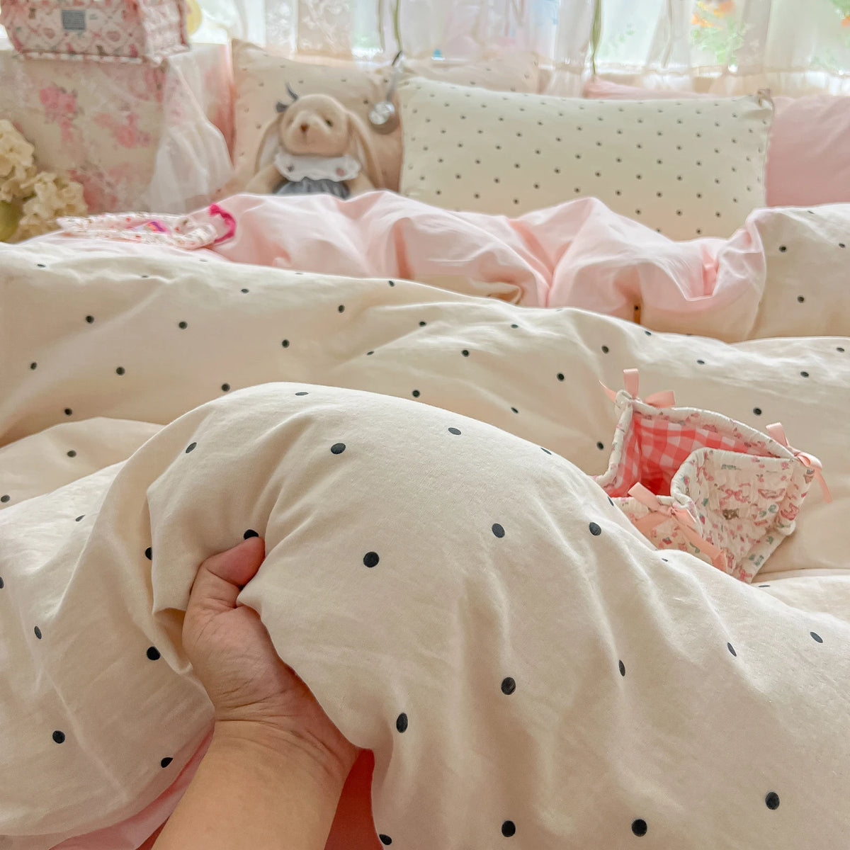 A close-up of a light pink polka dot duvet cover set with matching pillowcases and a hand touching the fabric.