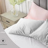 A set of silky soft pink and white pillowcases displayed on a bed with a wooden nightstand.