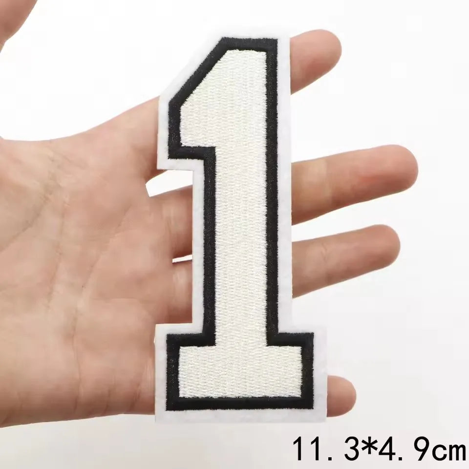 A hand holds a white letter patch shaped like the number one with black borders.