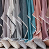 A close-up of various colored muslin throw blankets hanging together in a rack.