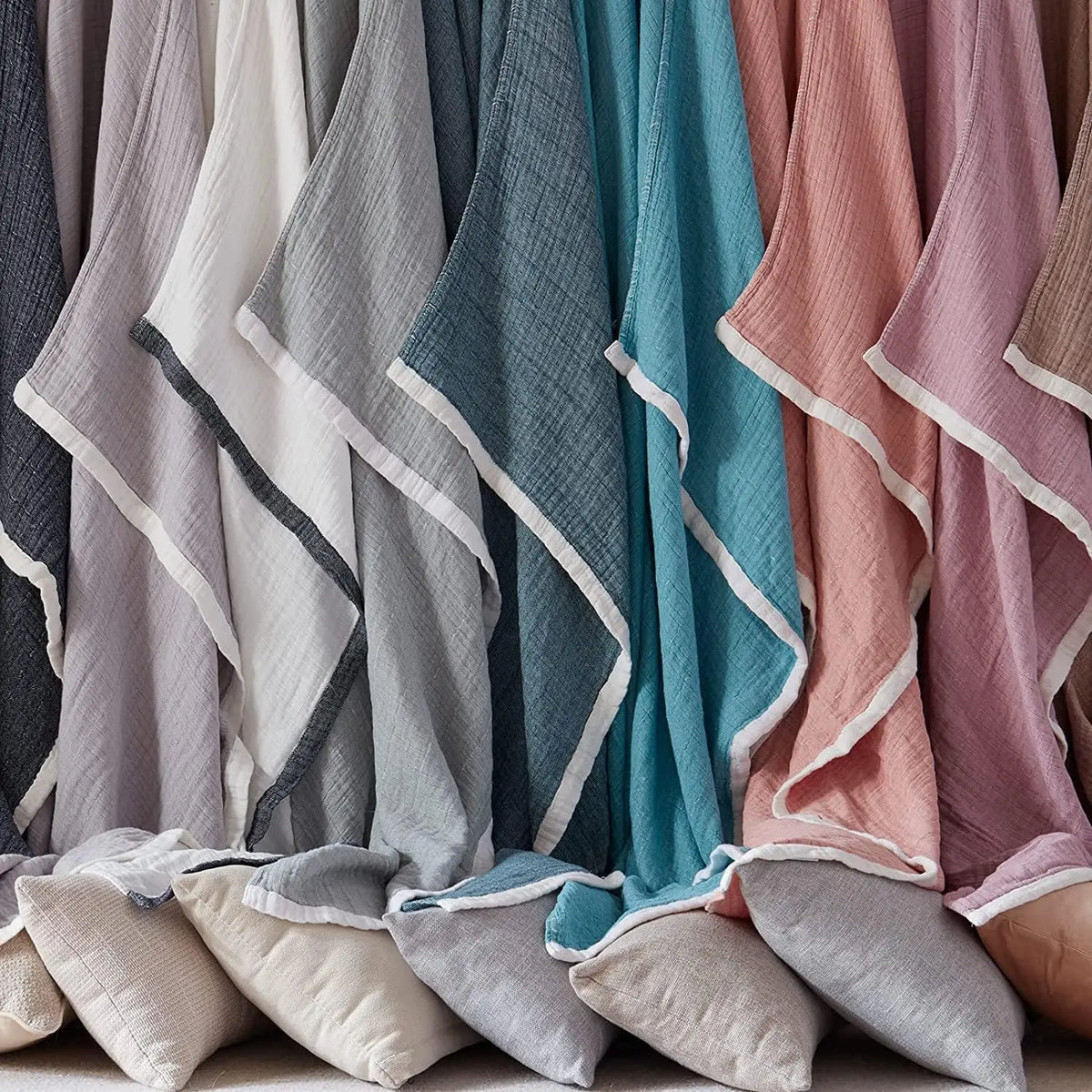 A close-up of various colored muslin throw blankets hanging together in a rack.