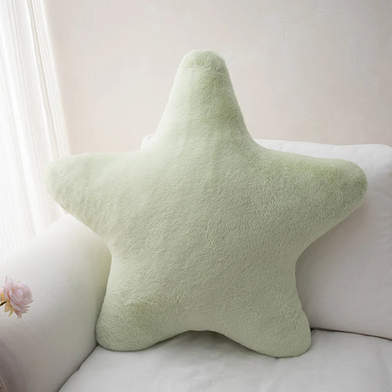 A light green star-shaped plush throw pillow resting on a white sofa.