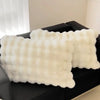 A white, fluffy quilted pillow cover is displayed on a dark surface.