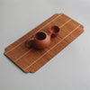 A terracotta teapot rests on a bamboo tea mat with woven stripes.