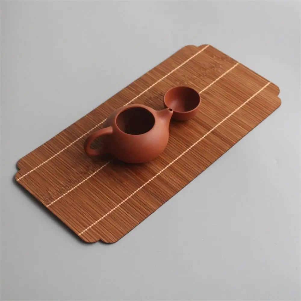 A terracotta teapot rests on a bamboo tea mat with woven stripes.