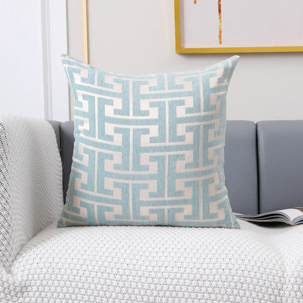 A light blue geometric jacquard lumbar pillow cover with a repeating maze pattern resting on a gray sofa.