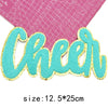 A turquoise glitter script letter cheer patch on a pink grid background.